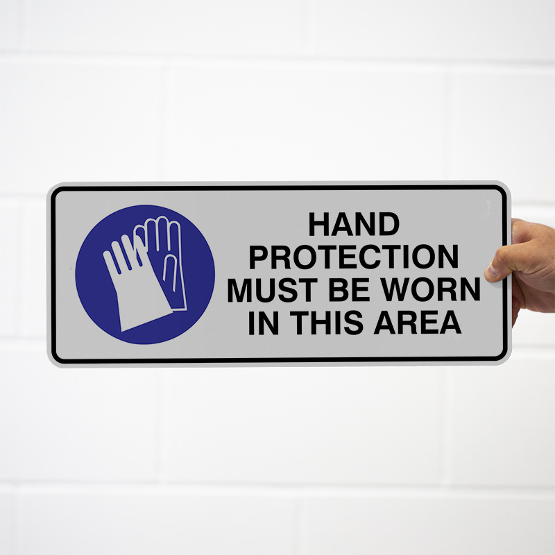 A sign indicating that hand protection must be worn in a designated area, featuring an illustration of gloves and written instructions in bold black text on a grey background with a blue circle.