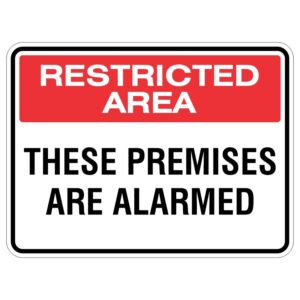 A sign displaying the text 'RESTRICTED AREA' in red on top and 'THESE PREMISES ARE ALARMED' in black below, indicating limited access and security measures.