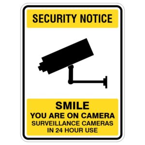 A security notice sign featuring a black silhouette of a surveillance camera, with the text 'SECURITY NOTICE' at the top, followed by 'SMILE YOU ARE ON CAMERA' and 'SURVEILLANCE CAMERAS IN 24 HOUR USE' at the bottom, all on a yellow background.